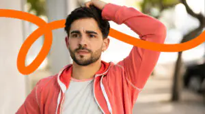 Portrait of a man with a trimmed beard in a coral hoodie, outdoors, with an orange curved branding swoosh across the image.