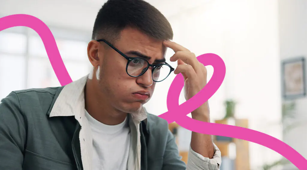 Young man with glasses sits at a desk in an office, looking puzzled and resting his hand on his temple with a pink abstract line in the background.