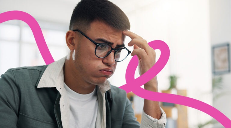 Young man with glasses sits at a desk in an office, looking puzzled and resting his hand on his temple with a pink abstract line in the background.